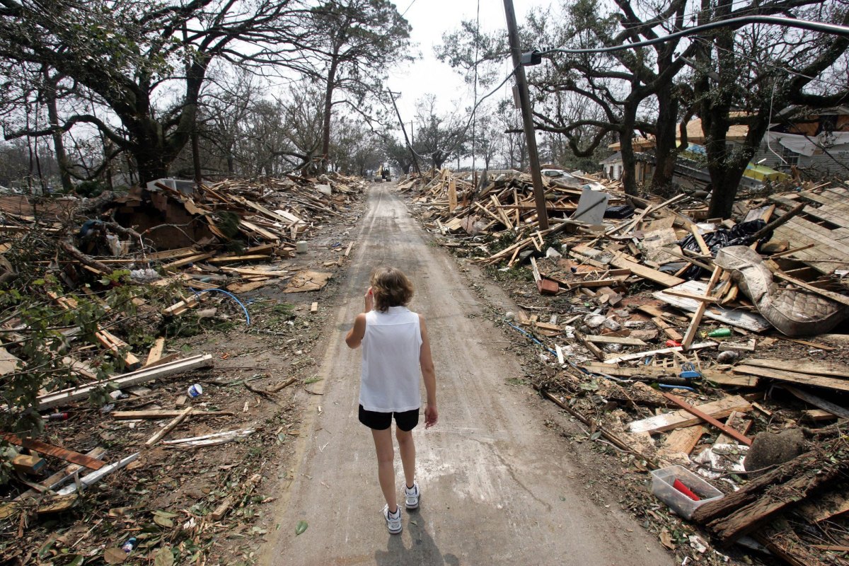 A woman walks down a cleared street between piles of homes reduced to rubble from a hurricane