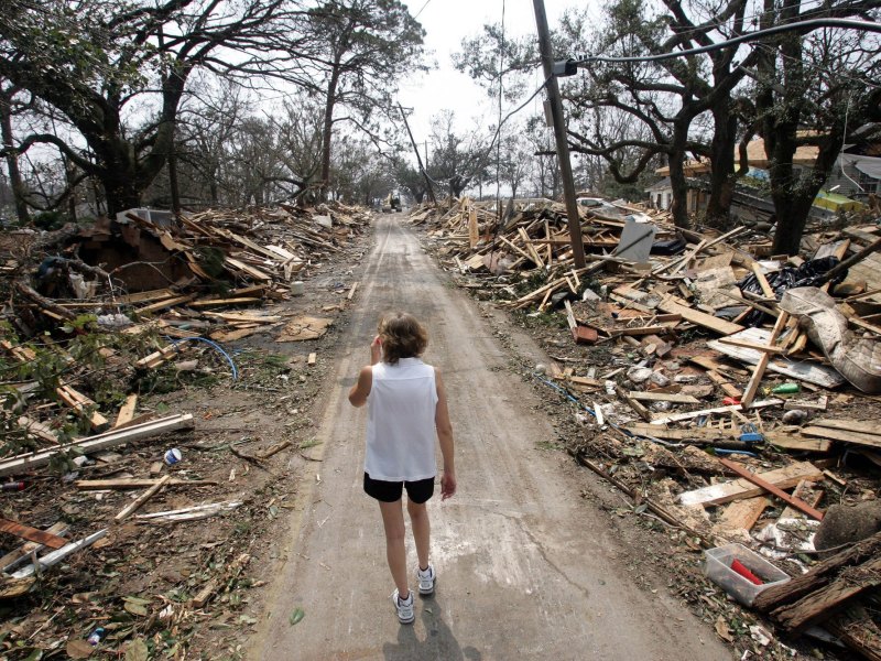 A woman walks down a cleared street between piles of homes reduced to rubble from a hurricane