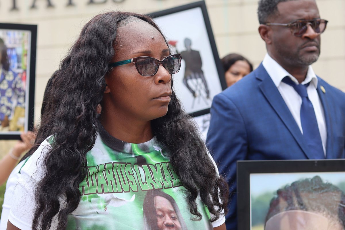 A woman at an outside press conference, wearing a green shirt showing Kadarius Smith