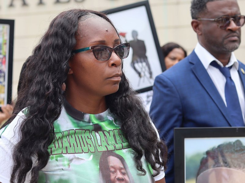 A woman at an outside press conference, wearing a green shirt showing Kadarius Smith