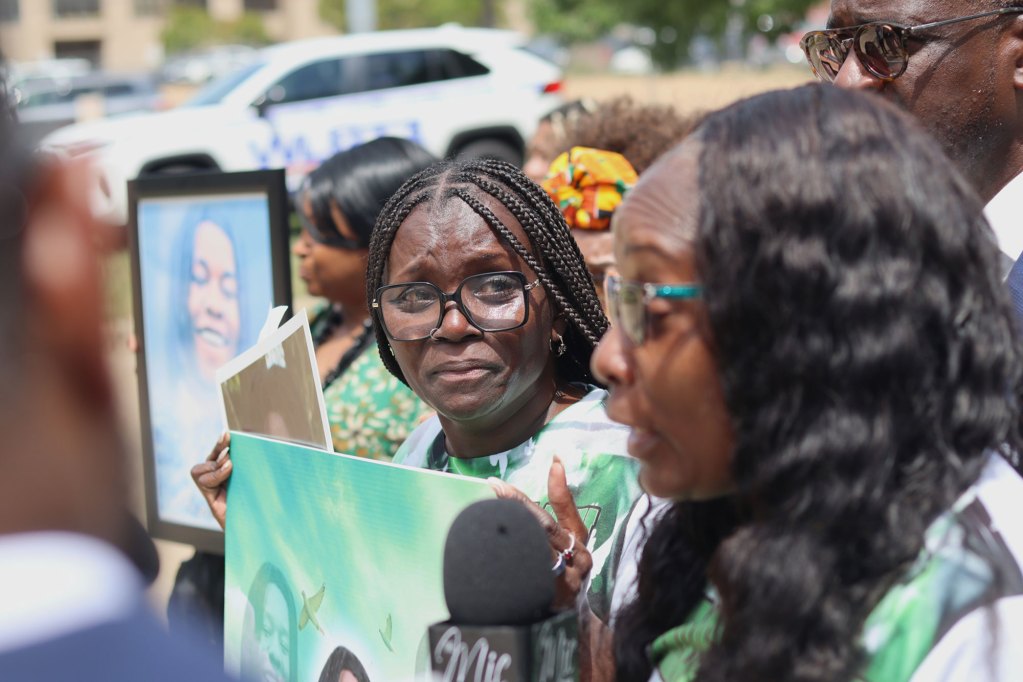 A tearful woman looks on at the speaker of an outside press conference