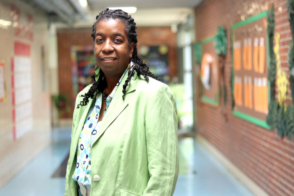 A person with twisted hair and wearing a light green suit stands in a school hallway