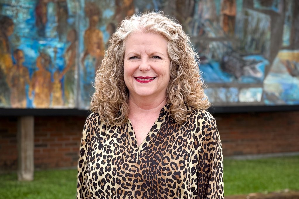 A blonde woman in cheetah print poses before a mural.