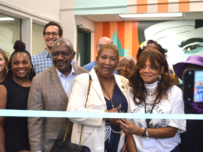 A group of people including John Horhn cut a blue ribbon in front o a mural of Medgar Evers