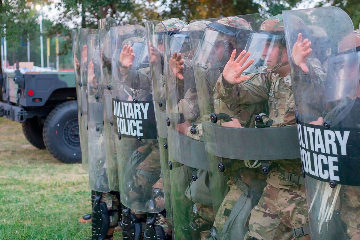A row of men in camouflage uniforms hold up shields that read 'Military Police'