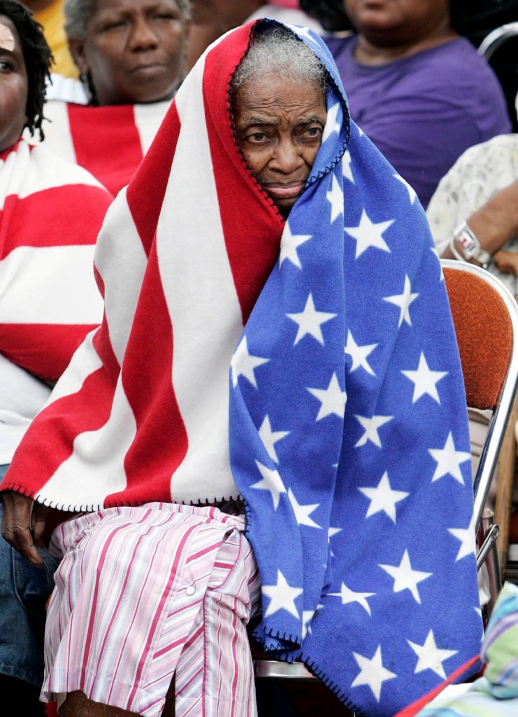 an elderly black lady has an american flag blanket wrapped around her head and body