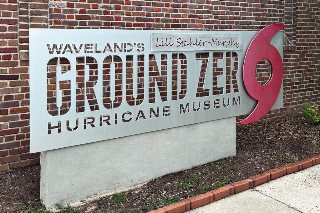 A steel sign that reads 'Waveland's Ground Zero Hurricane Museum' with a red hurricane symbol on the right