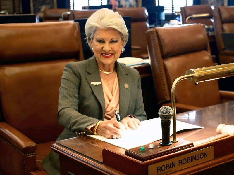 Robin Robinson sitting at her desk in the Senate signing a paper