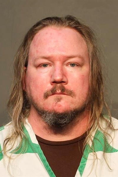 A mugshot of a longhaired man in white and green scrubs