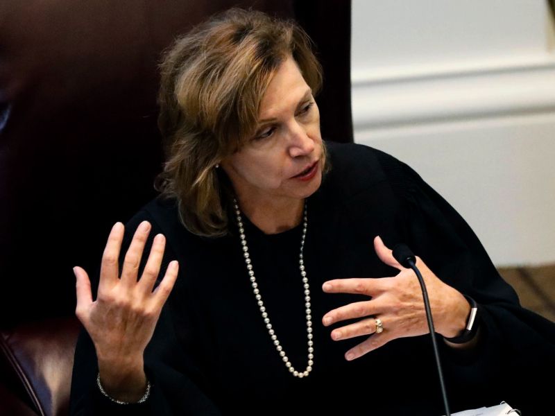 A judge in robes sits and speaks at her desk