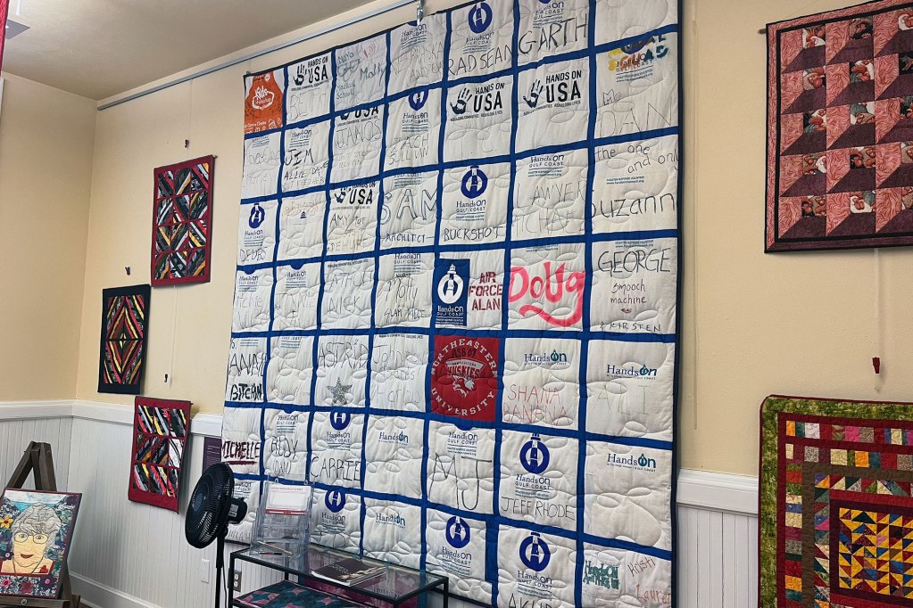 A large quilt hangs on a wall, surrounded by smaller fiber art pieces