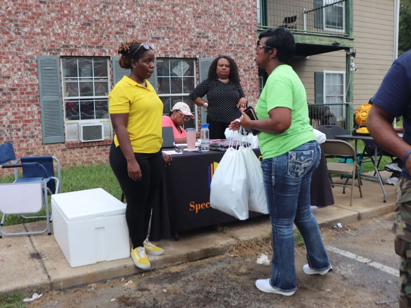 Various people sit and stand around a table set up outside of an apartment building