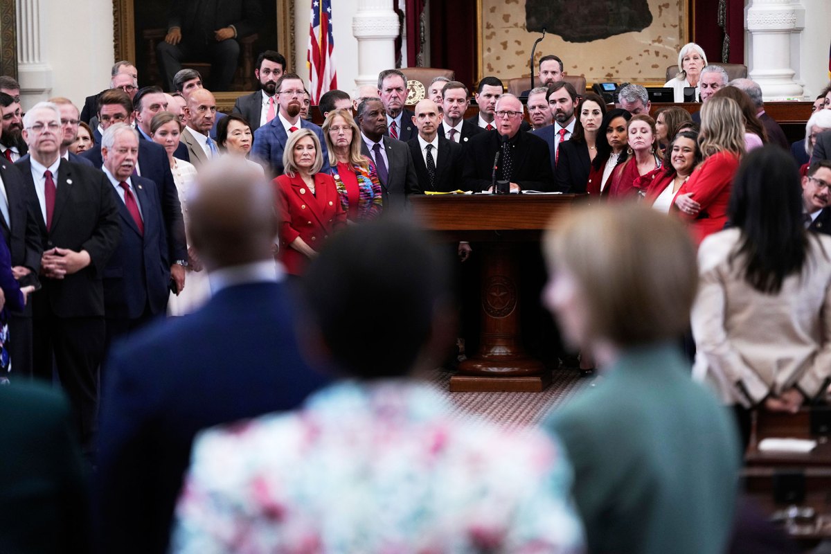A crowd of legislatures stand together on one side of a room