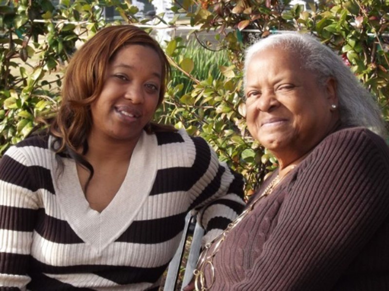 A woman and her daughter sit together on a bench outside