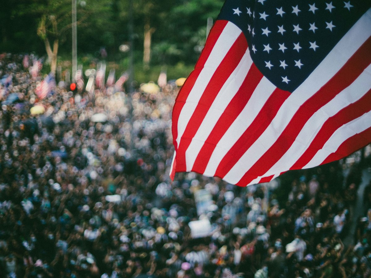 A US flag seen waving outside over a blurry crowd of people