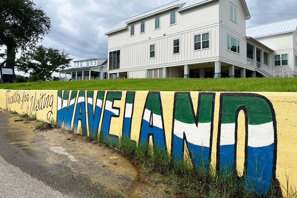 A mural reads 'Thanks for Visiting Waveland' by the sidewalk of a neighborhood