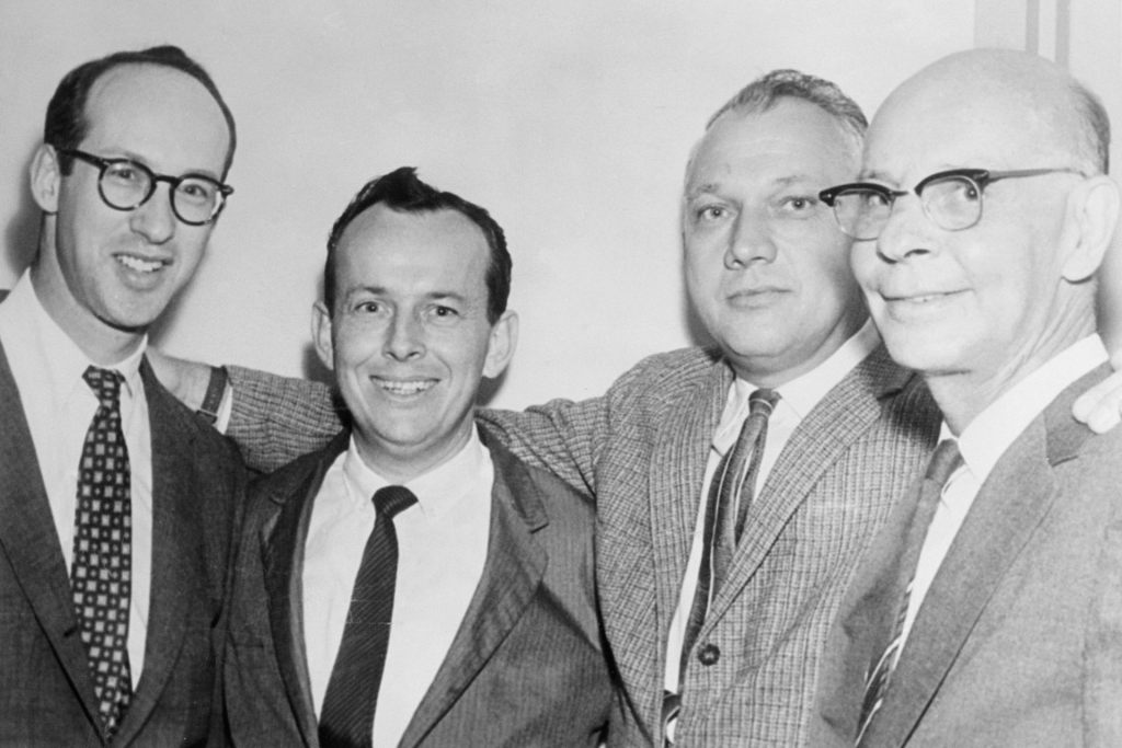 Four men in suits standing together and smiling