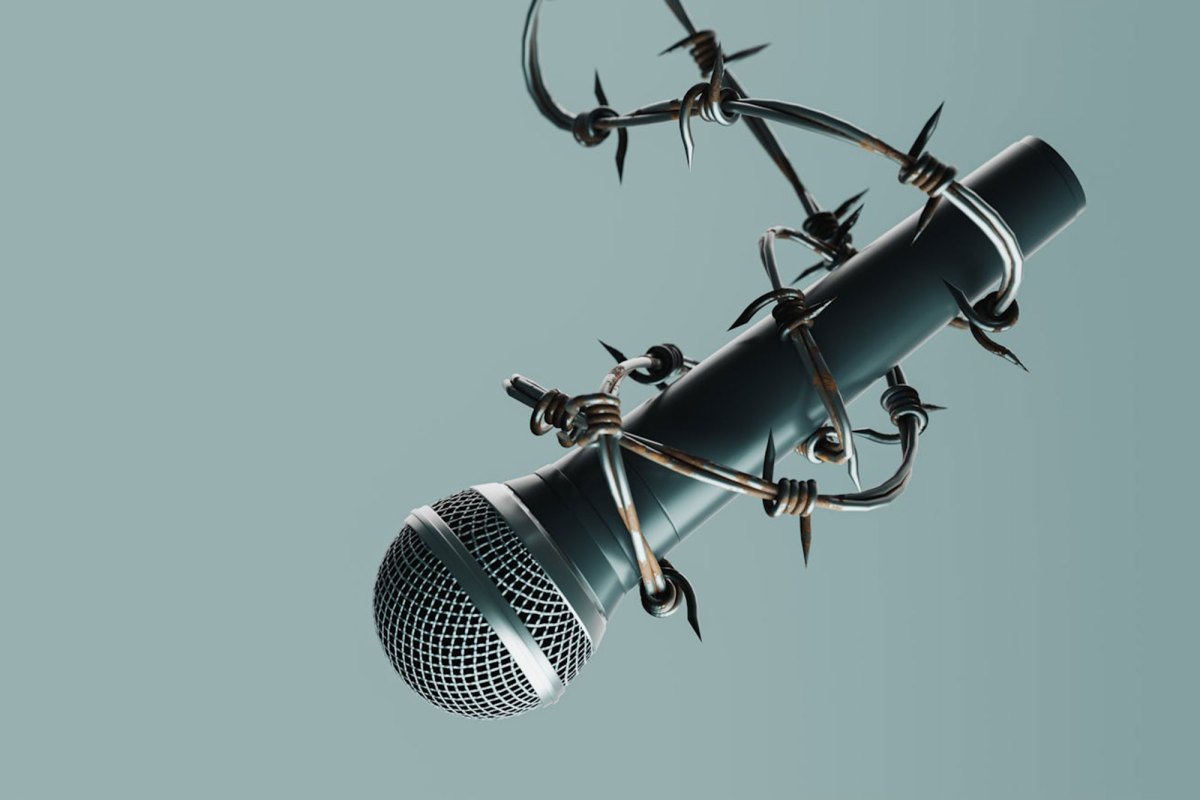 A microphone suspended by barb wire against a sage green background