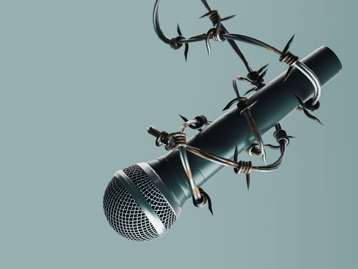 A microphone suspended by barb wire against a sage green background