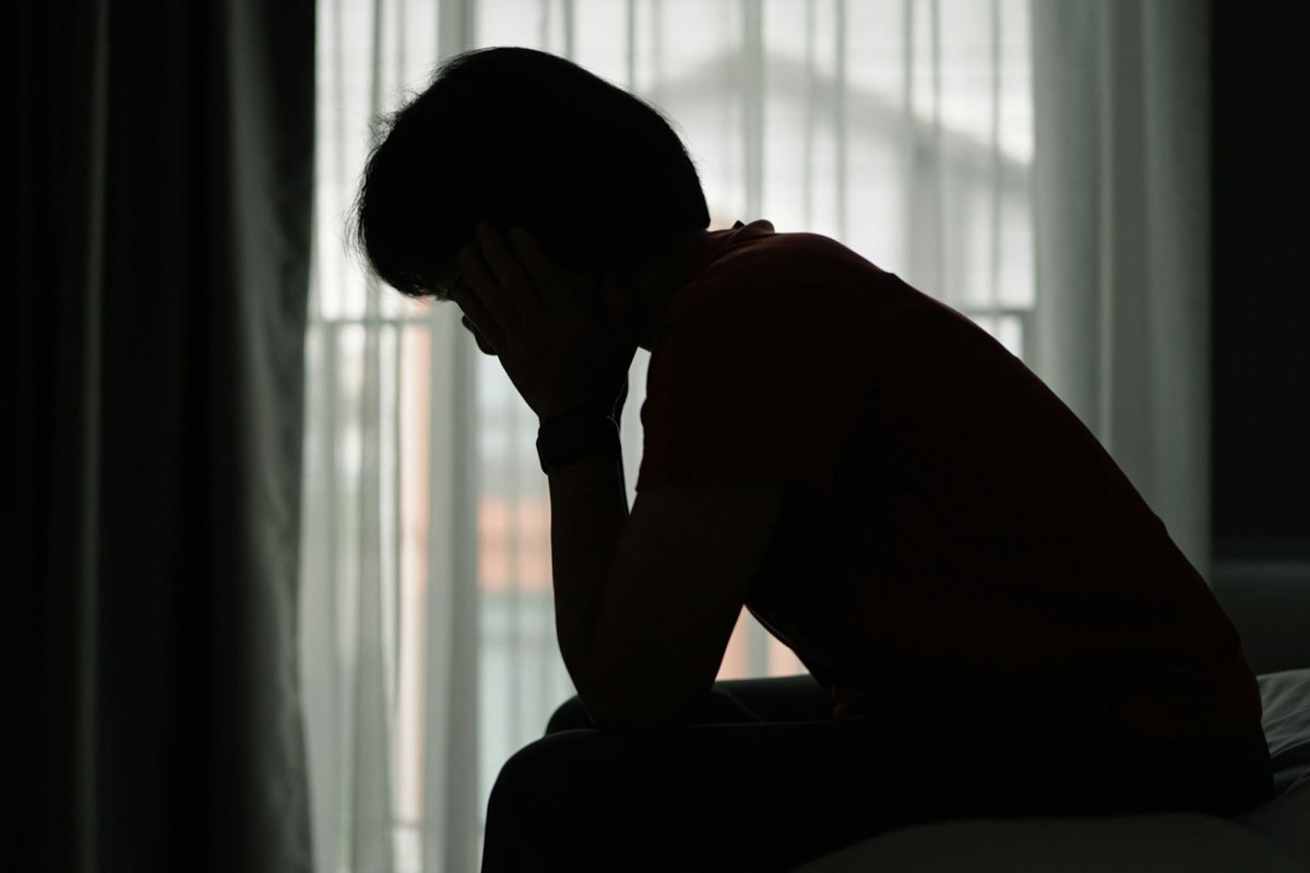 The silhouette of a woman sitting on the edge of her bed in front of a window, head in hands