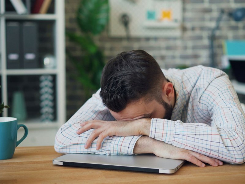 A man sitting at a desk with his head in his hands, leaning on a closed laptop
