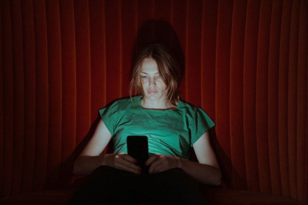 A woman siting on a couch, lit by the light of her cell phone screen