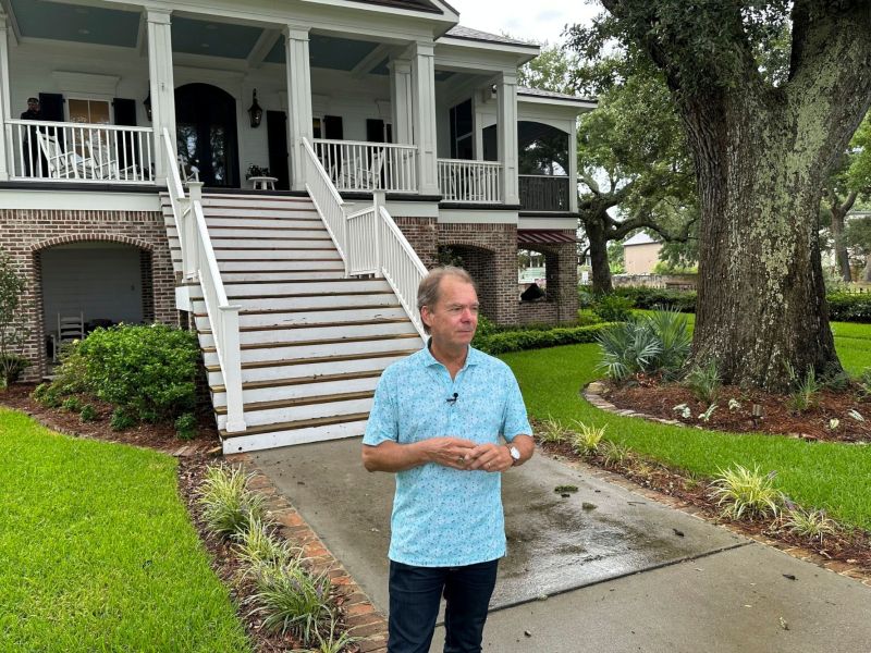 Billy Hewes stands in front of his stilted brick home