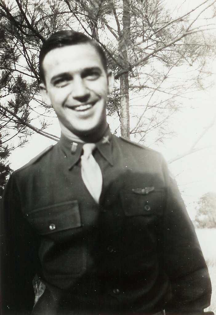 An old black and white photo of a smiling man standing outside in army uniform