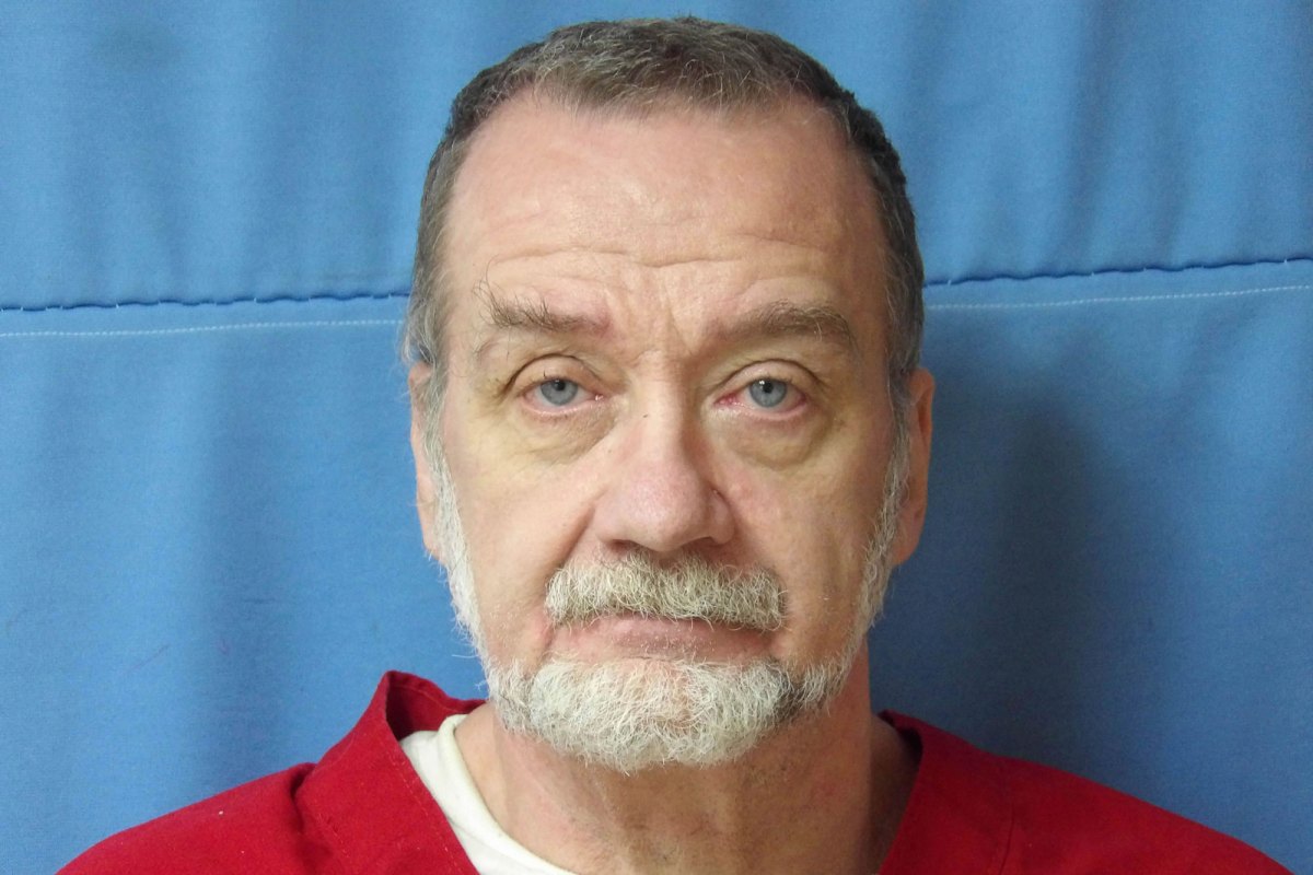 Mugshot of a man in a red jumpsuit standing in front of a blue wall