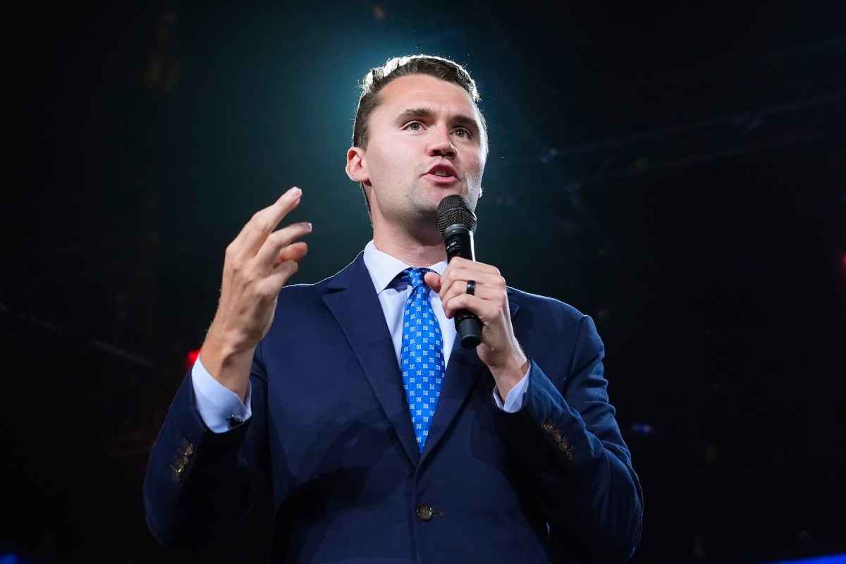 Charlie Kirk holding a microphone on a black stage