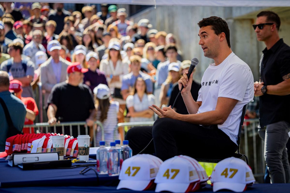 Charlie Kirk seen seated, speaking at an outdoors gathering