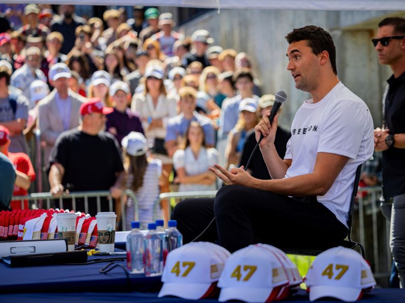 Charlie Kirk seen seated, speaking at an outdoors gathering