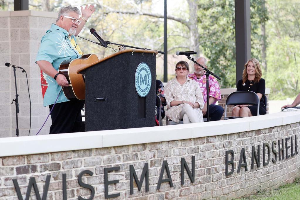 Craig Wiseman stands at a podium for an event, guitar in hand.