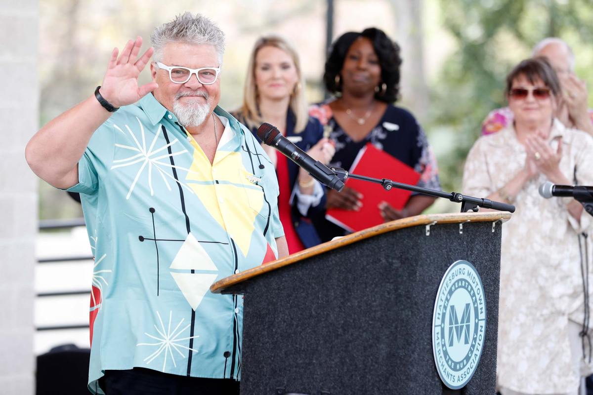 Craig Wiseman waves at a podium for an event as people clap behind him