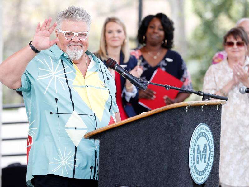 Craig Wiseman waves at a podium for an event as people clap behind him