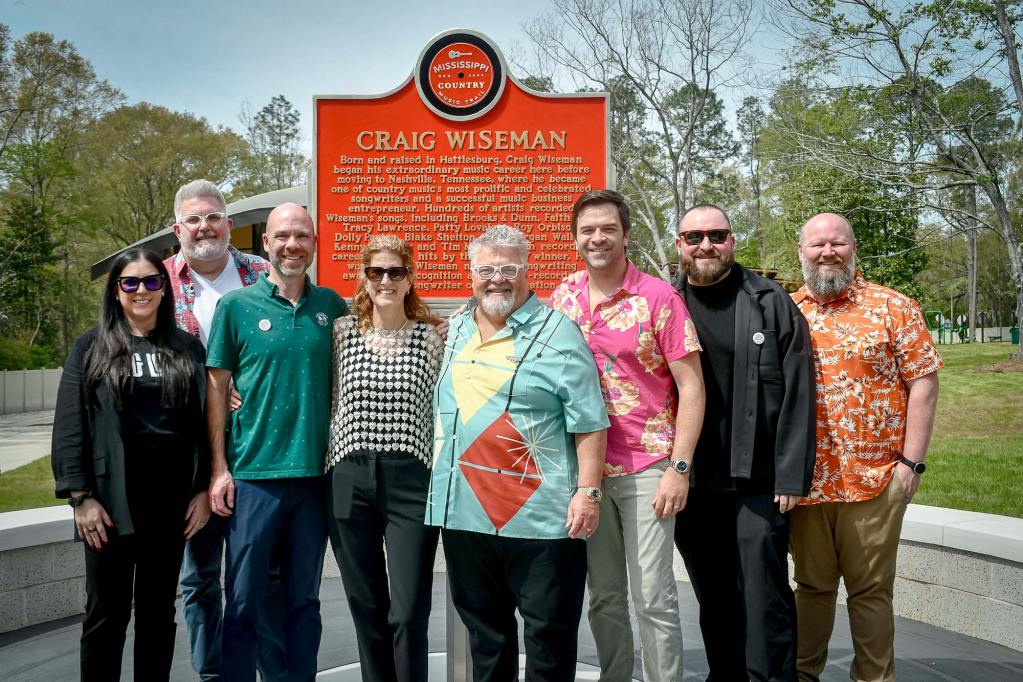 Eight people stand in front of a red marker labeled 'Mississippi Country Music Trail - Craig Wiseman'