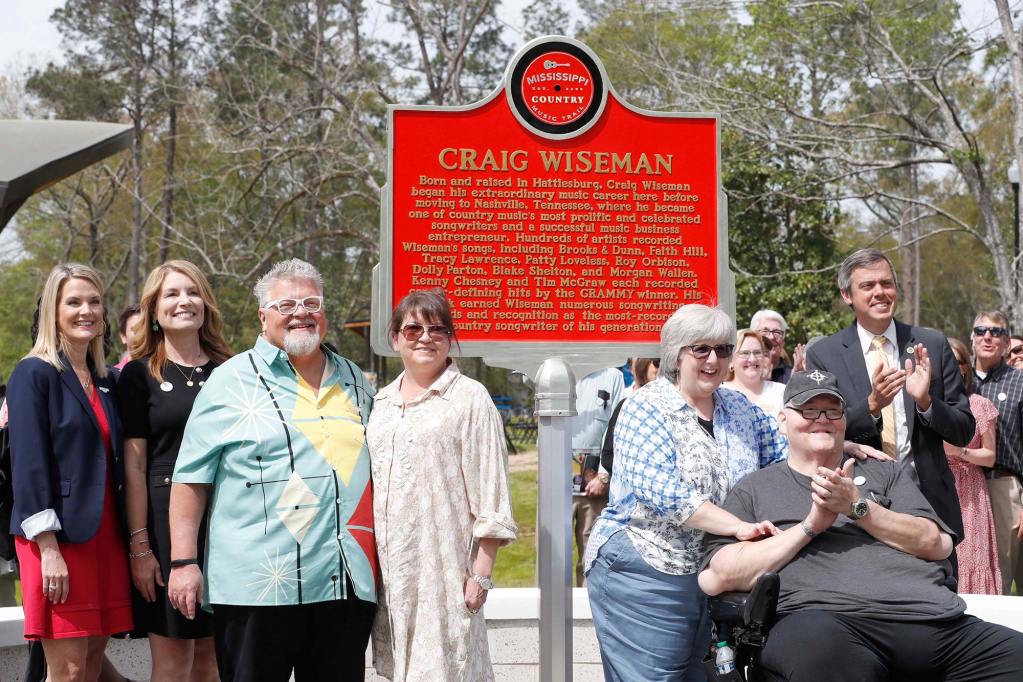Many people stand around a red marker labeled 'Mississippi Country Music Trail - Craig Wiseman'