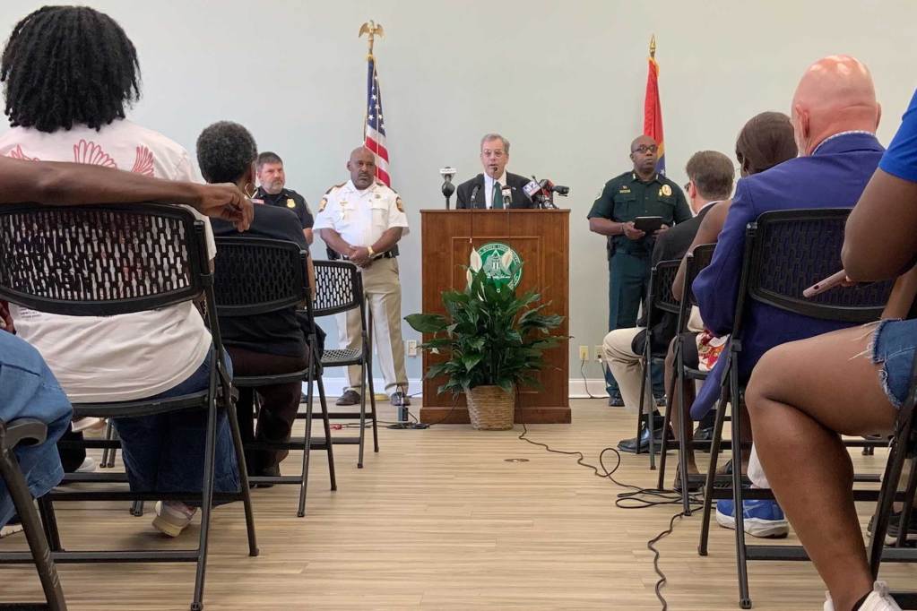 A man speaks at a podium at a press conference as a seated audience listens