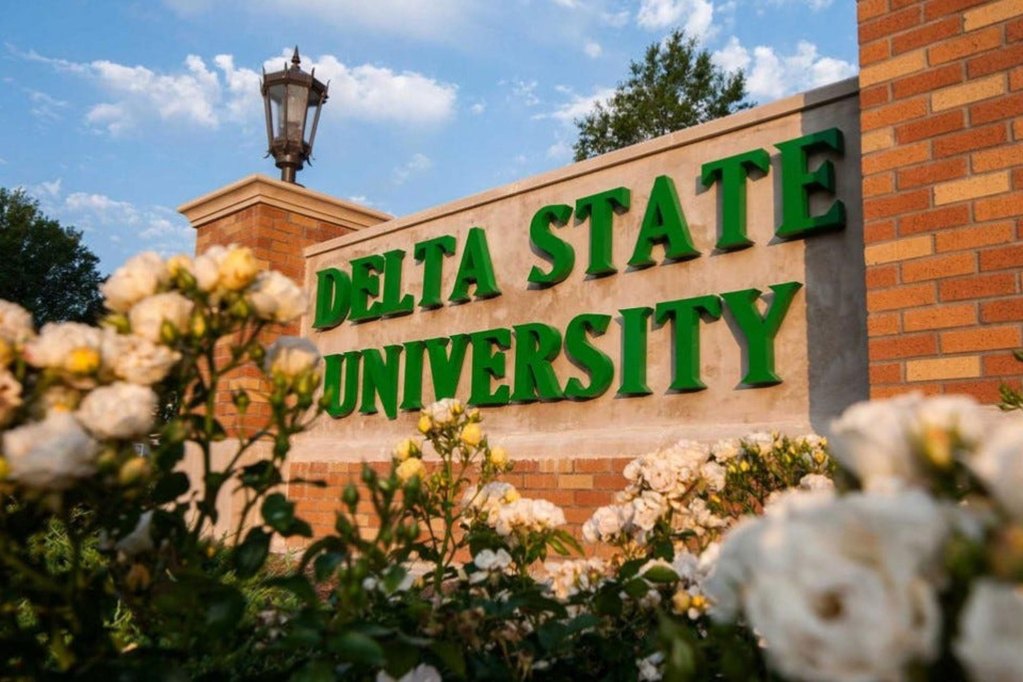 An exterior sign surrounded by white roses that reads 'Delta State University' in green letters