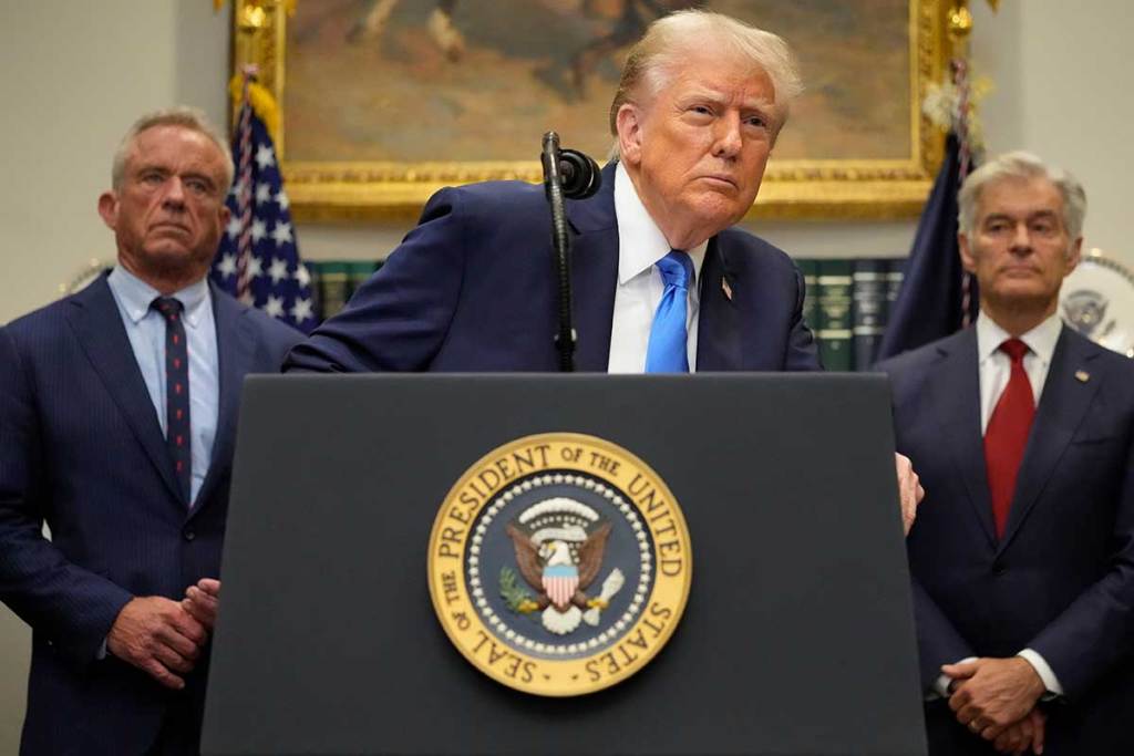 Donald Trump, at a White House podium, leans to listen to a question