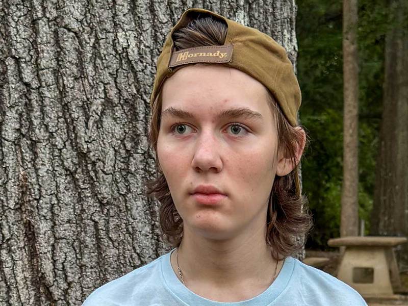 A teenage boy wearing a backwards baseball cap stands outdoors