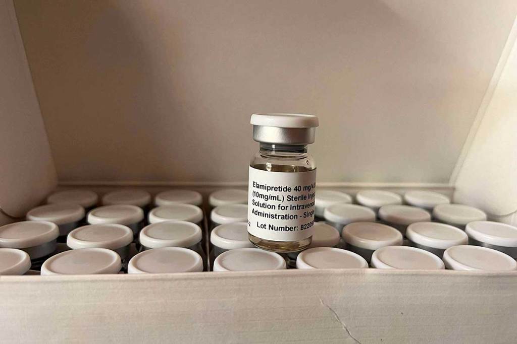 A small glass vial labeled “Elamipretide” sits among other vials in a box.