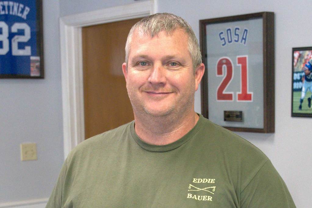A man in a green shirt smiles and stands inside a local store.
