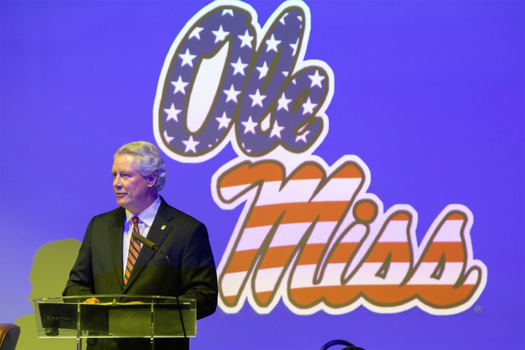 Glenn Boyce stands on stage with an Ole Miss logo projected on the wall behind him