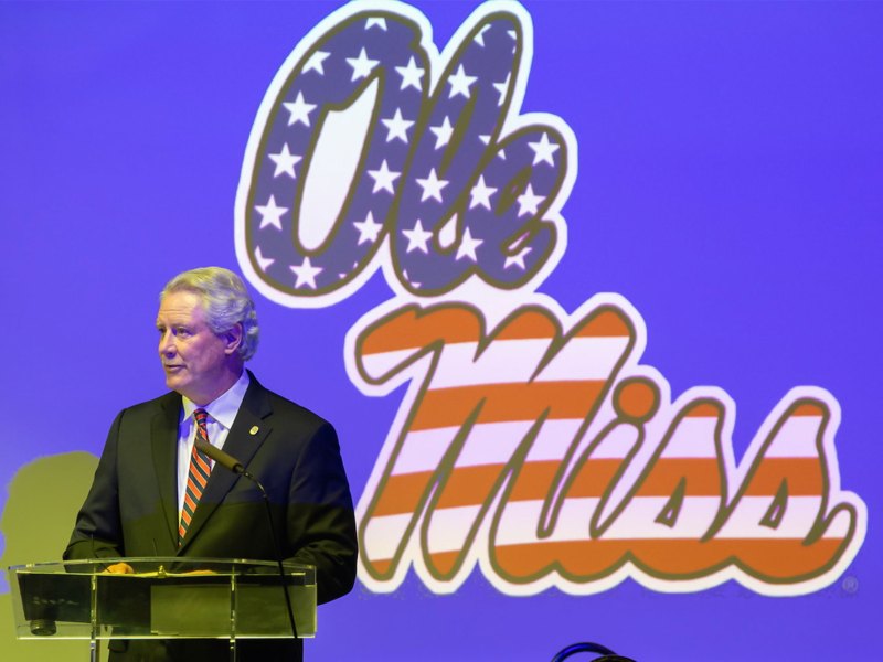 Glenn Boyce stands on stage with an Ole Miss logo projected on the wall behind him
