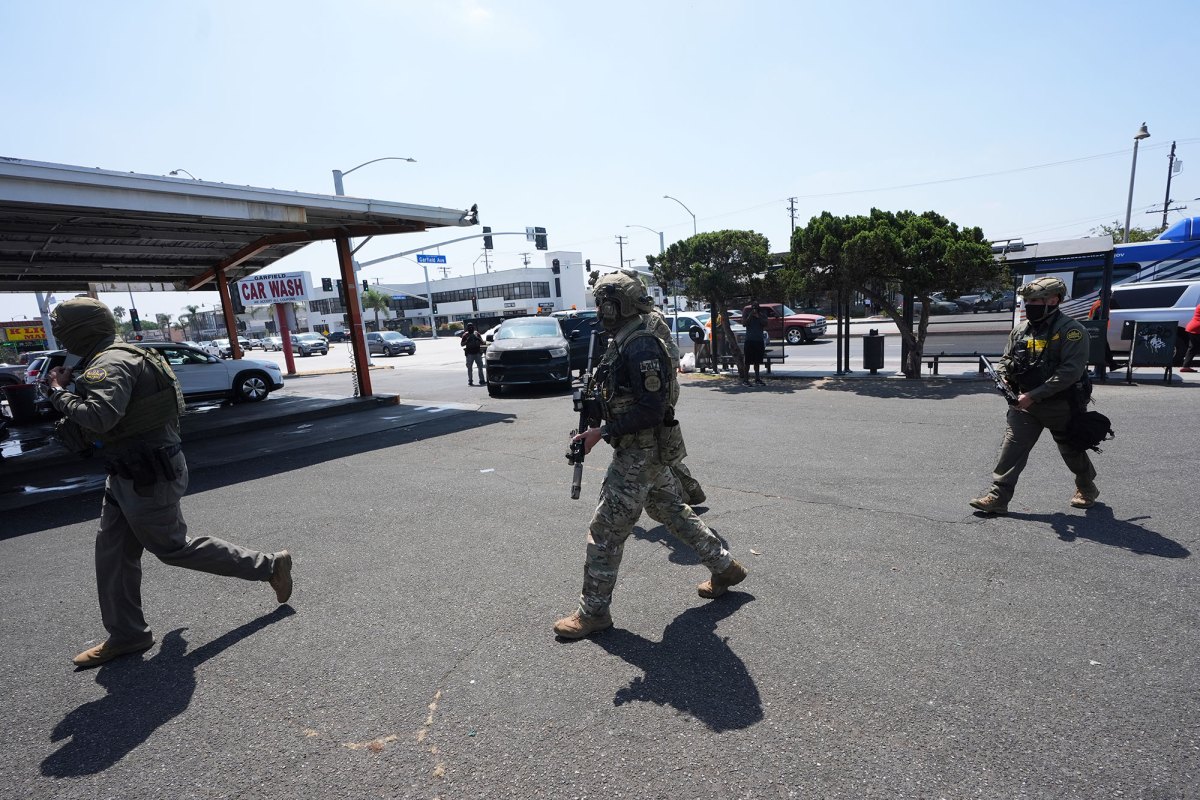 Three armed people in camo gear stalk across a car wash