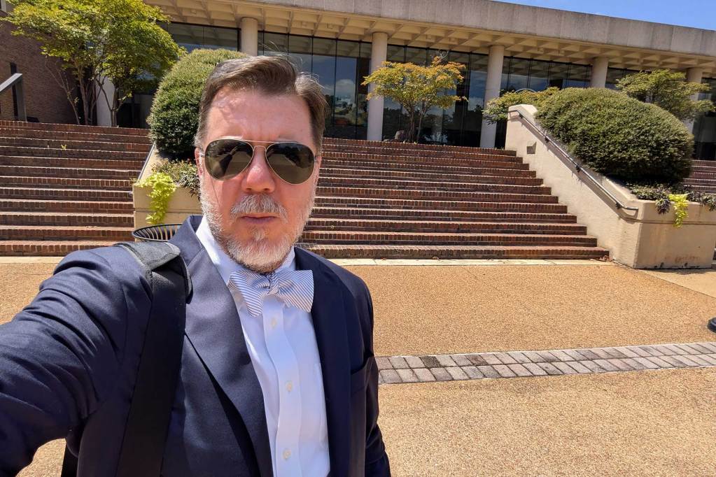 Jeffrey Baker in a selfie showing a university building behind him