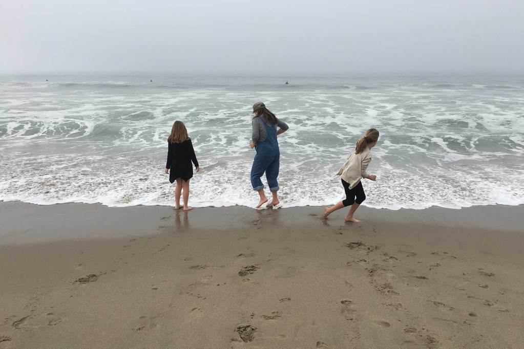 Three people stand in the waves at a beach