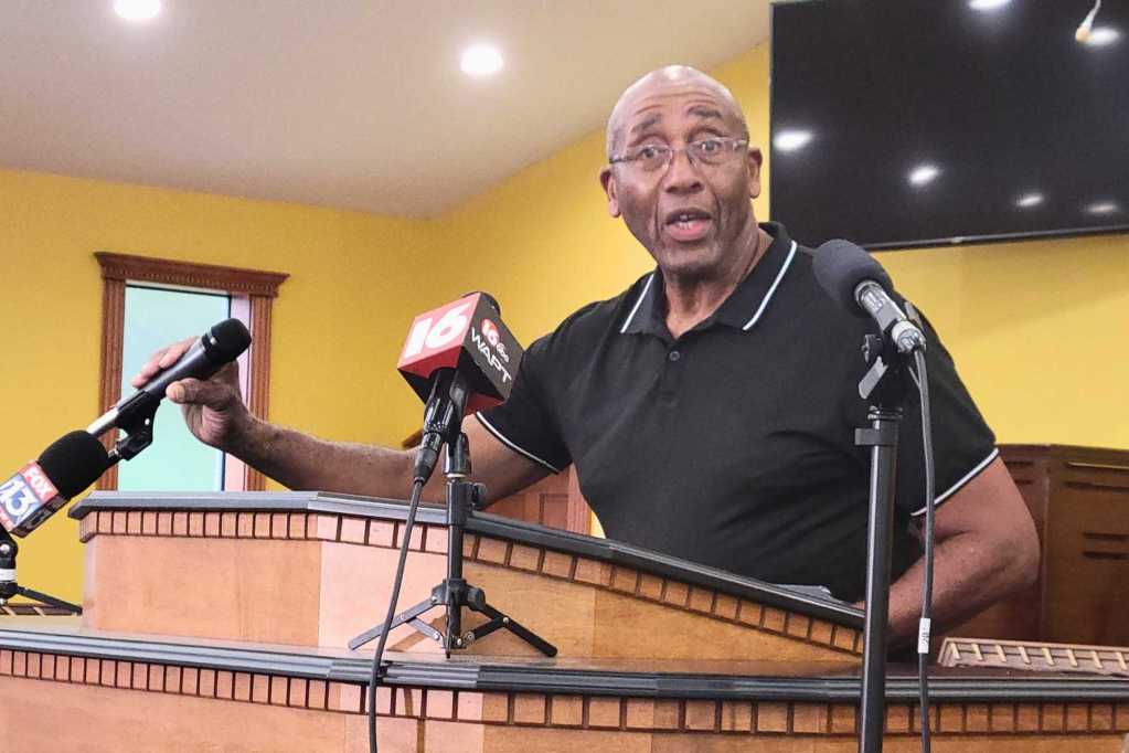 A man speaking at a press conference held in a church with yellow walls