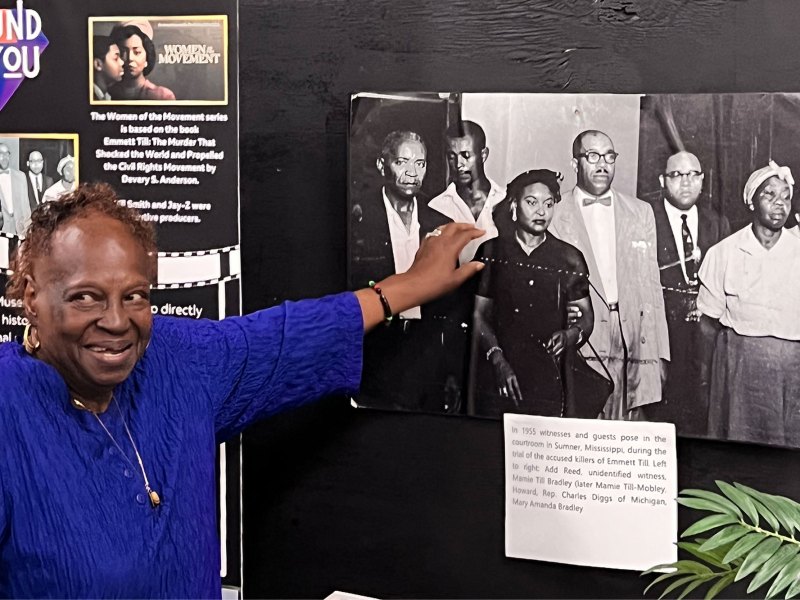 A woman points to an old black and white photo in an exhibit